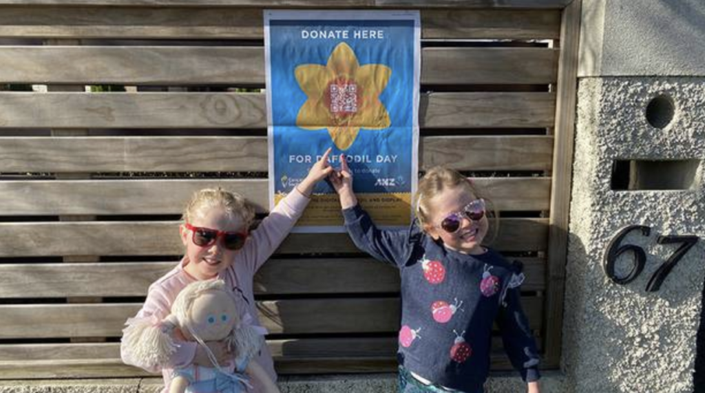 two young supporters of ANZ Daffodil Day pointing to a fundraising poster